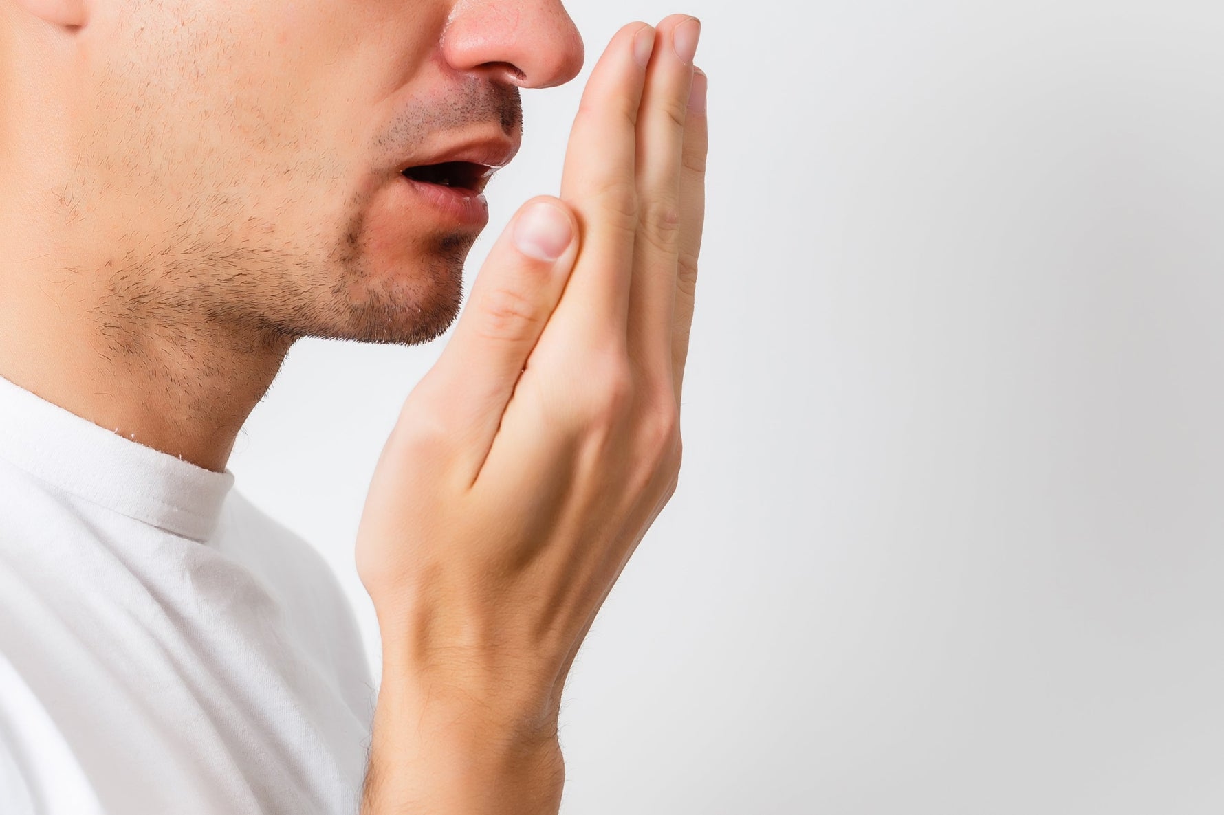 A man is breathing into his hand to check his breath.