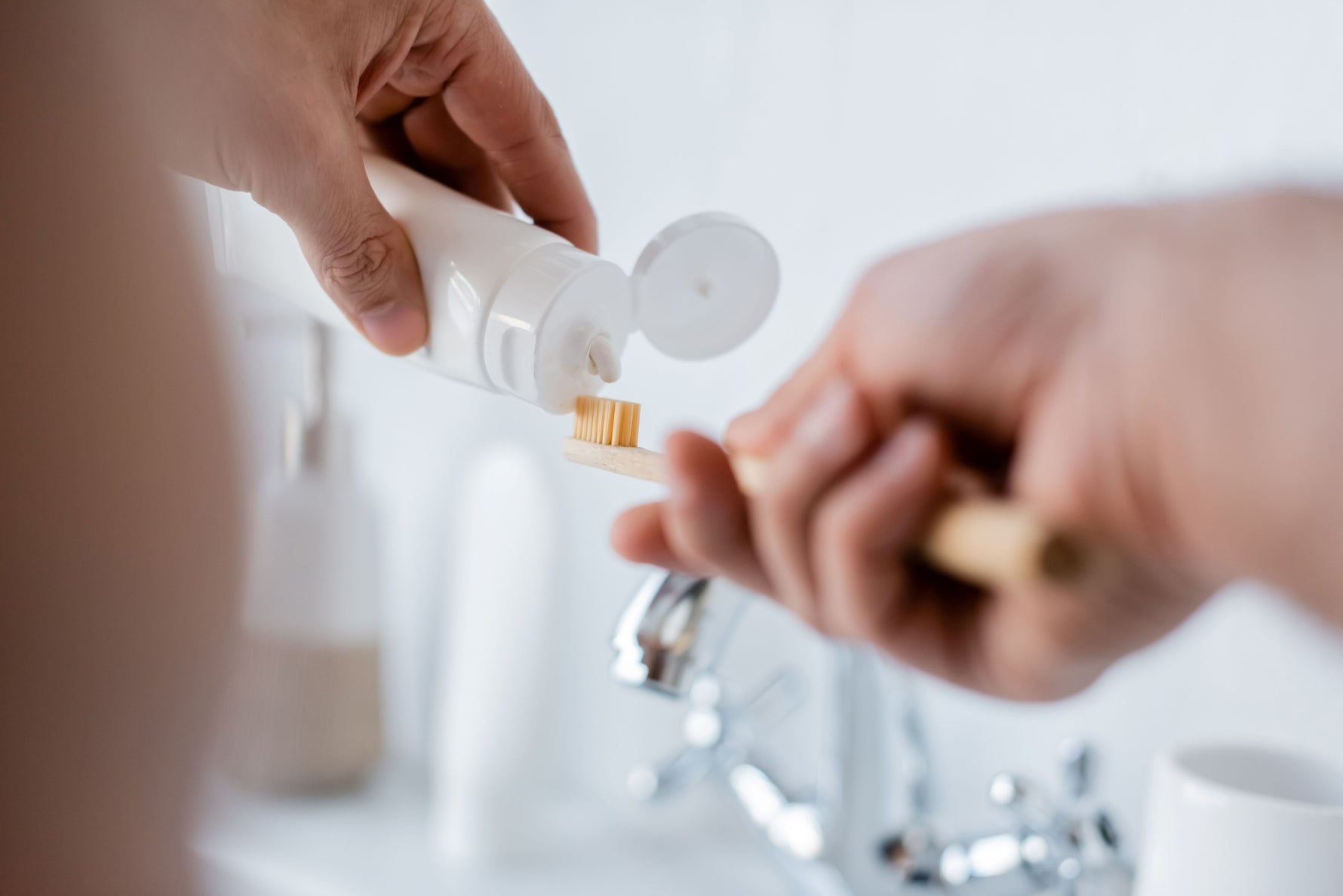 A person applying toothpaste onto a toothbrush over a sink.