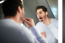 A middle aged man with brown hair looking in the mirror looking in the mouth, pulling his lip