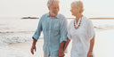 An older man and lady holding hands walking on the beach